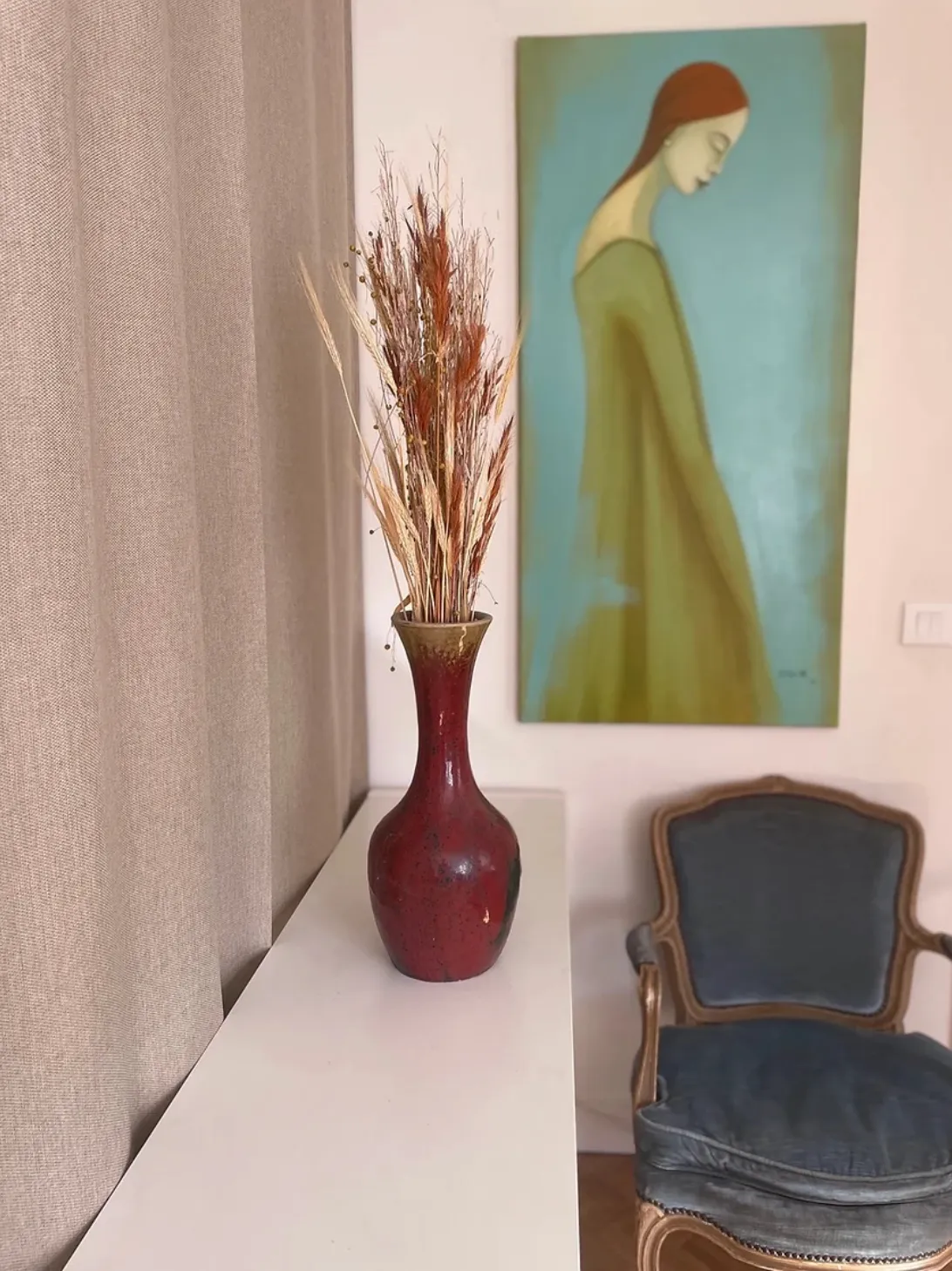 Un coin de la salle d’attente : console avec bouquet séché, fauteuil et tableau